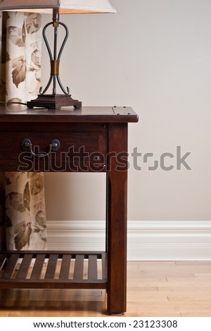 Solid wood end table with lamp against earth tone wall and hardwood floor.