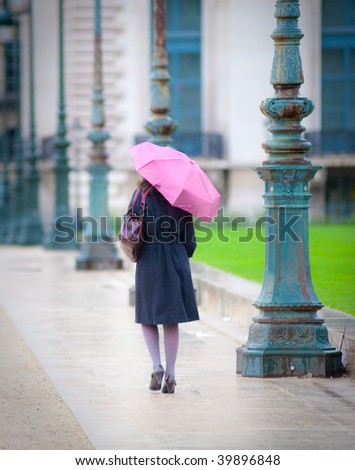 Young woman walks down sidewalk under umbrella in the rain.