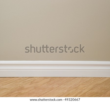 Interior design detail. Beige wall, clean white baseboard molding and wooden floor.