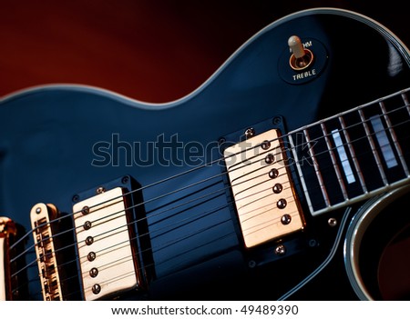 Classic black Les Paul rock and roll or jazz style guitar. Soft blue lighting on guitar and warm background light creates stage or studio performance atmosphere.
