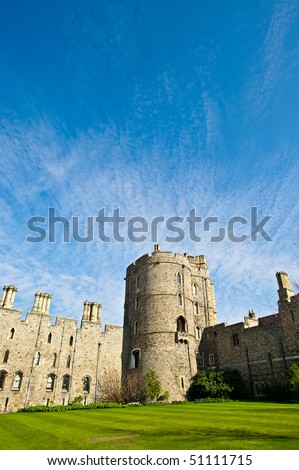 Historic English castle with blue sky and green lawn. This is Windsor Castle, the oldest and largest occupied castle in the world and home to Queen Elizabeth II.