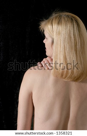 Upper back of beautiful, sexy blonde woman on black background rubbing and massaging her back or neck pain