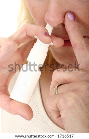 Close-up of woman spraying nasal spray in nostril and holding other nostril for effectiveness.