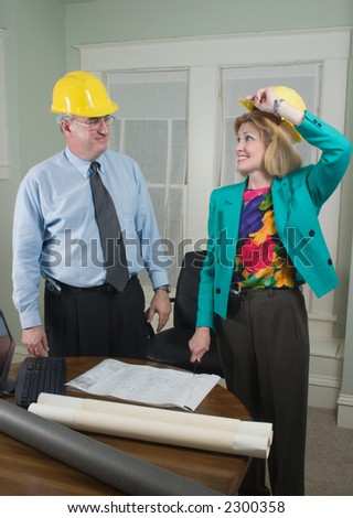 Architect showing client blueprints in the office.  Wearing hardhats in preparation for a visit to the construction site.