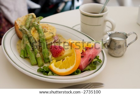 Beautiful culinary preparation of eggs benedict breakfast at popular restaurant in tourist area. Focus on strawberry and orange slice with rest of the scene out of focus from depth of field effect.