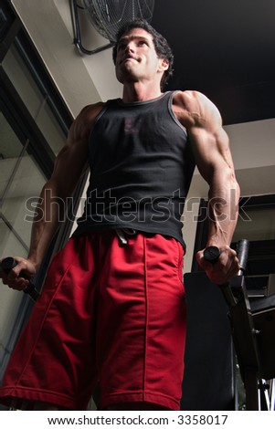 Man, with a determined expression on his face, exercising his arm muscles on an exercise machine in a fitness center.