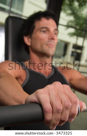 Closeup of a man\'s hand on an arm exercise machine in a fitness center.  The hand is in clear focus with shallow depth of field causing the man\'s face to be out of focus.