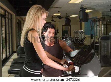 Man and woman exercising together at a fitness center on a treadmill walker exercise machine.  Man could be a personal fitness trainer.