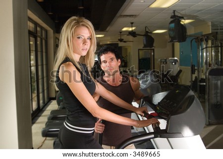 Man and woman exercising together at a fitness center on a treadmill walker exercise machine.  Man could be a personal fitness trainer. Woman is in focus with man slightly out of focus.