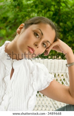 Portrait of a beautiful young brunette woman with her hair pulled back sitting comfortably outside on a love seat on the porch.