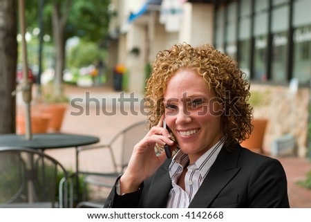 Smiling business woman relaxing on the sidewalk while discussing business on a cellphone.