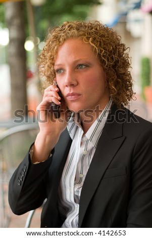 Serious business woman relaxing on the sidewalk while discussing business on a cellphone.