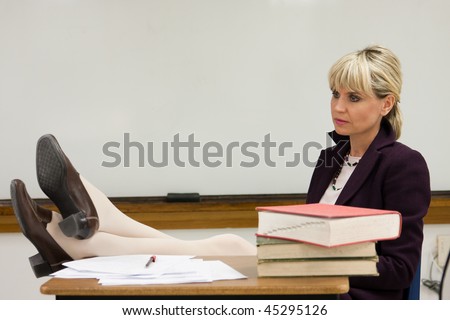 Woman teacher or instructor in a college, university, high school, middle school, elementary classroom relaxing with her feet up on her desk.