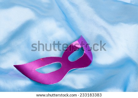 Purple carnival mask lying on blue silk fabric