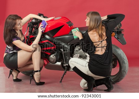 Two young girls wash a bike, on red background