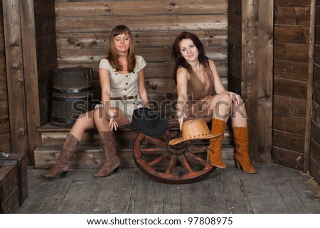 brunette and blonde CowGirls with a ancient cart wheel sitting in old depot