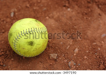 A well used yellow softball on the infield dirt.