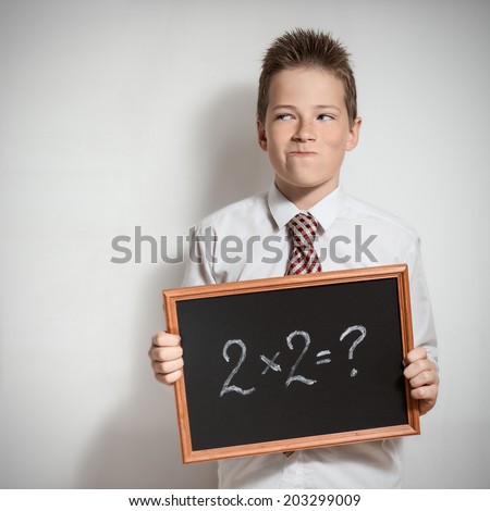 The cute smiling schoolboy teenager in a white shirt thinking about the task decision on the black chalkboard