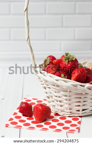Ripe strawberry in the white basket with red polka-dot napkin on the light grey brick and wooden background