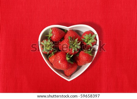 strawberries in a heart shaped bowl on a red textured place-mat