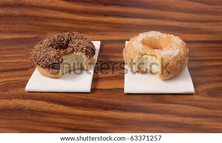 two doughnuts on napkins with bites missing on an office desk