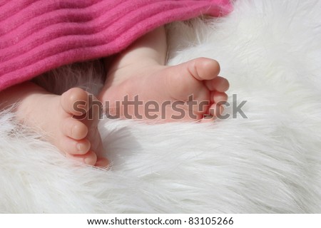 Tiny baby feet under pink blanket lying on white fur