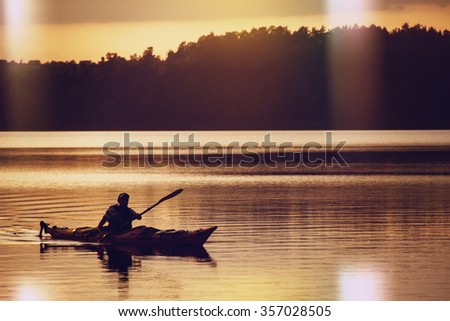 The man rowing oars in boat of kayak type on the lake at early evening. Golden sunset.Summer time, active recreation. Healthy lifestyle and care about mental health, resting in  privacy and peace.