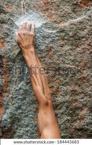 Closeup details of young and strong climbers hand gripped on a chalked wall. Detailed colorful rock and strong muscular hand.