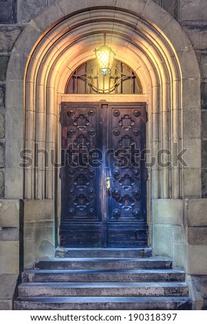 Old Medieval wooden door to church with stairs with lantern at night