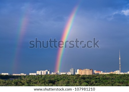 Double rainbow under city park in dark blue sky