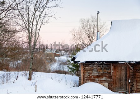 snow-covered wooden house in country at pink winter sunset