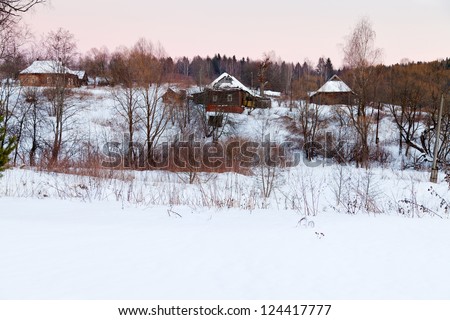 rural landscape with snowy wooden houses in country at pink winter sunset
