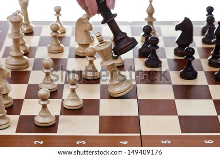 hand with black king hits white king on chessboard in chess game