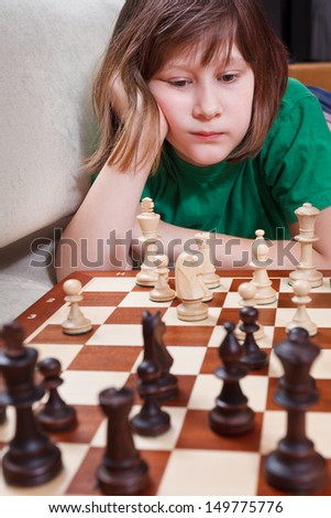 little girl thinking over chess game lying on couch