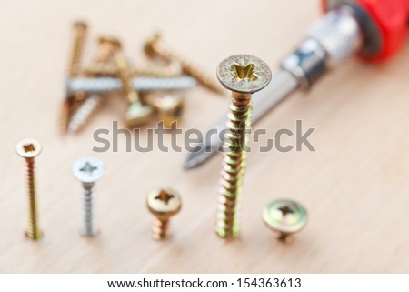 screwdriver and screws wrapped in wooden plank close up