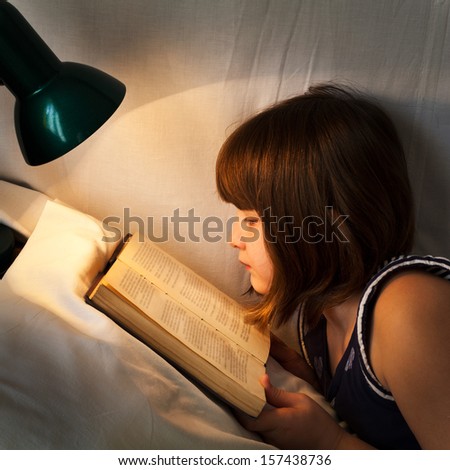 girl reading book on bed at night by light of lamp on bed