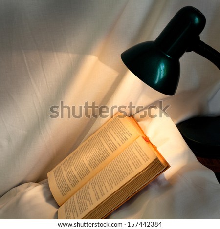 book on pillow lit reading lamp at night