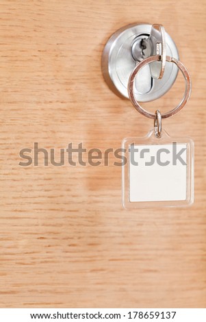 steel key with blank square keychain in lock of wooden door