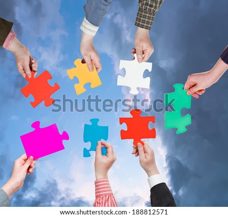 circle of people hands with different puzzle pieces with dark grey evening sky background