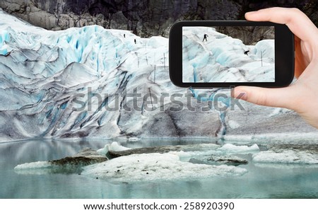 travel concept - tourist taking photo of people on briksdal glacier in Norway on mobile gadget