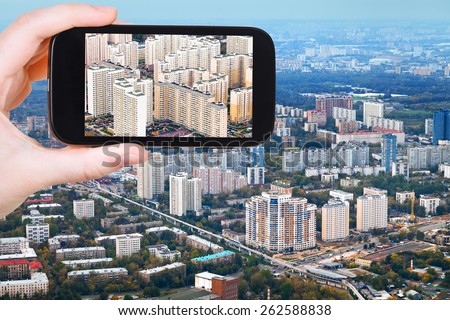 travel concept - tourist takes picture of block of modern houses in Moscow autumn day on smartphone,