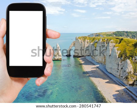travel concept - tourist photograph english channel coast with cliffs of Etretat cote d albatre, France on smartphone with cut out screen with blank place for advertising logo