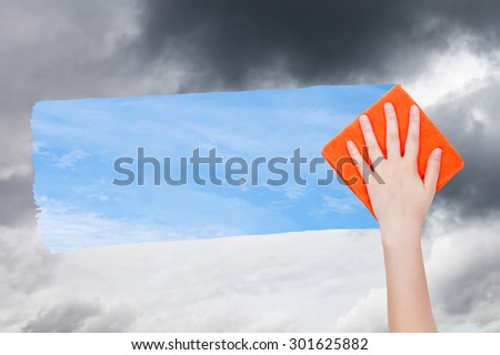 weather concept - hand deletes dark clouds by orange cloth from image and blue sky with white clouds are appearing