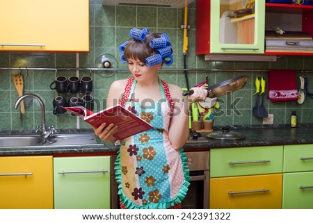 The young housewife in an apron and hair curlers on kitchen with a frying pan