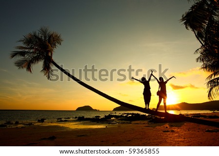 happy time, two girl stand on coconut tree on the beach with sunset time , Thailand, Asia