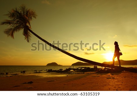 A girl stands by the palm tree on the beach at sunset , Thailand, Asia