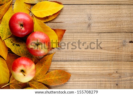 Three apples on autumn leaves on wooden background