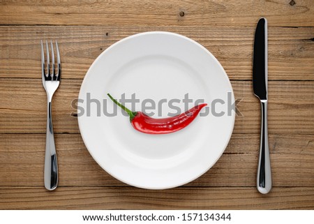 Red pepper on plate, fork and knife on wooden background