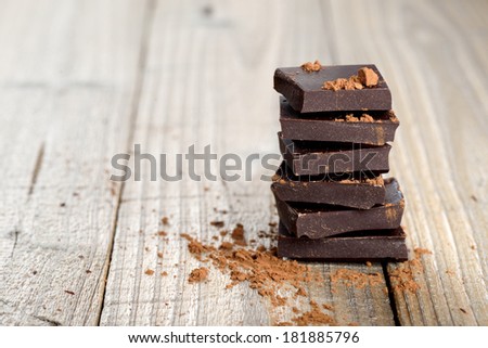 Pile of chocolate pieces with cocoa on wooden background