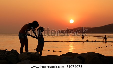 Silhouettes of child and his mother against orange sunset at sea